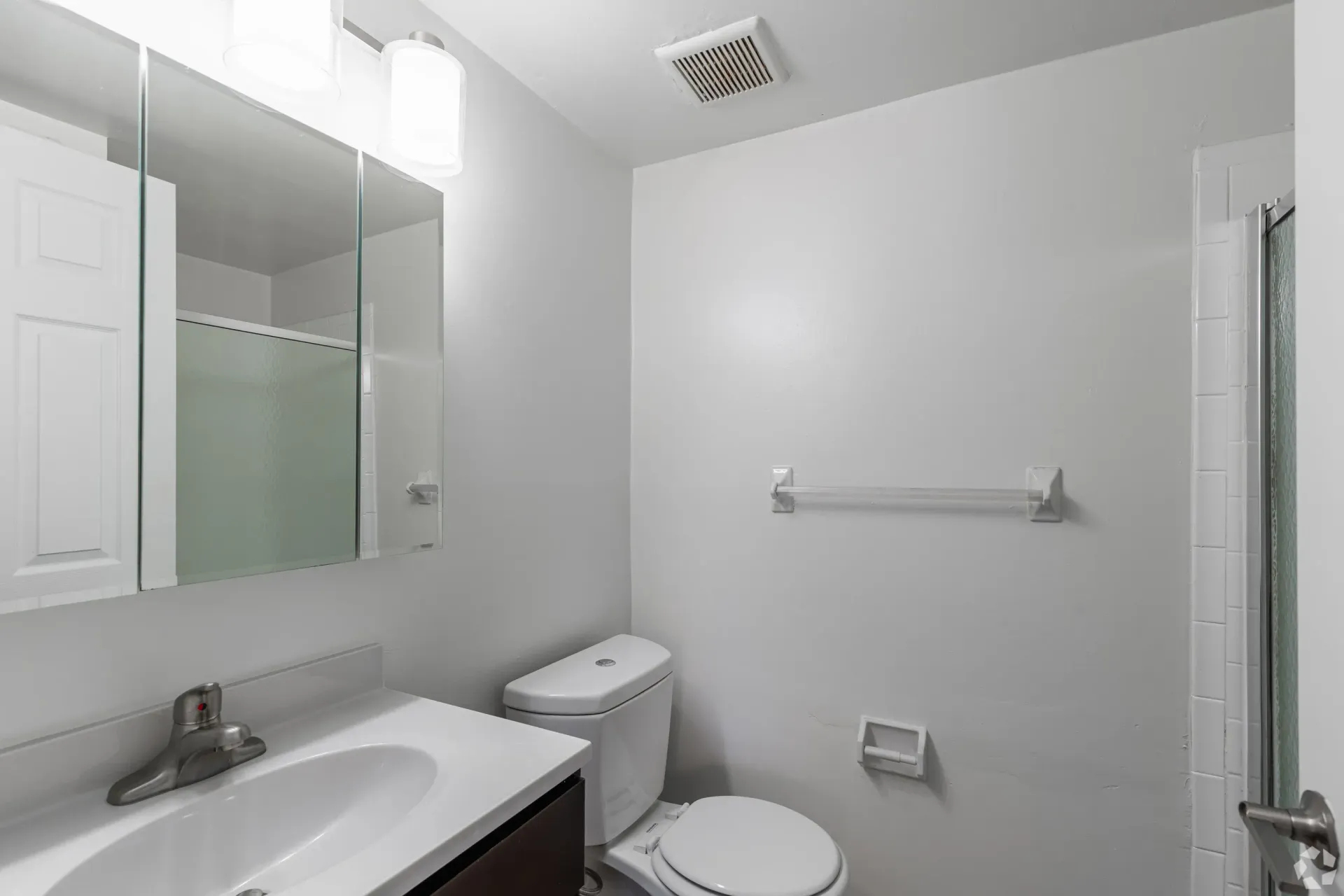 Small bathroom in a modern apartment with sink, medicine cabinet mirror, toilet, and shower at Liberty Pointe in Newark, DE.