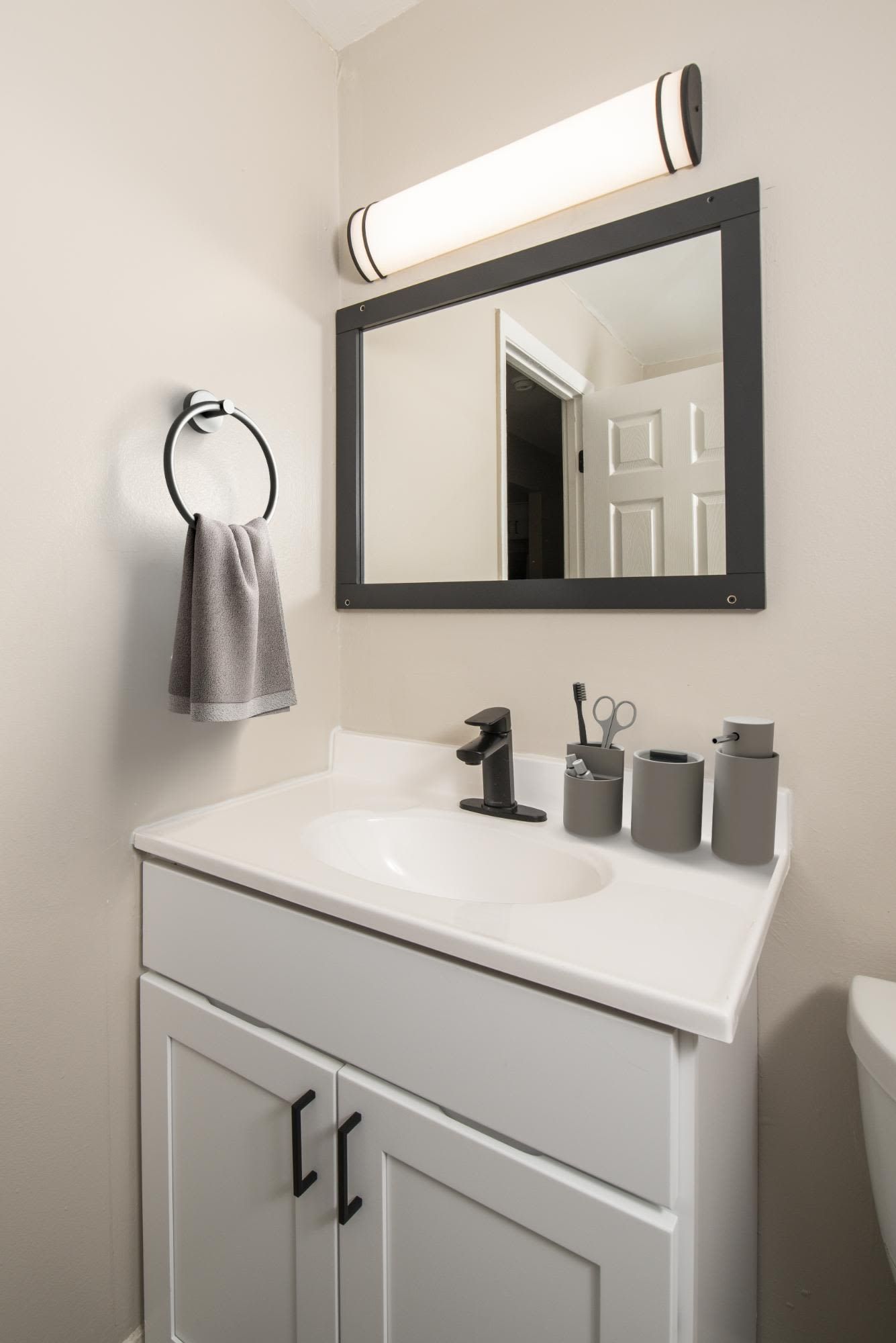 Bathroom vanity with white sink, black faucet, large framed mirror, towel ring, and gray accessories at Liberty Pointe in Newark, DE.