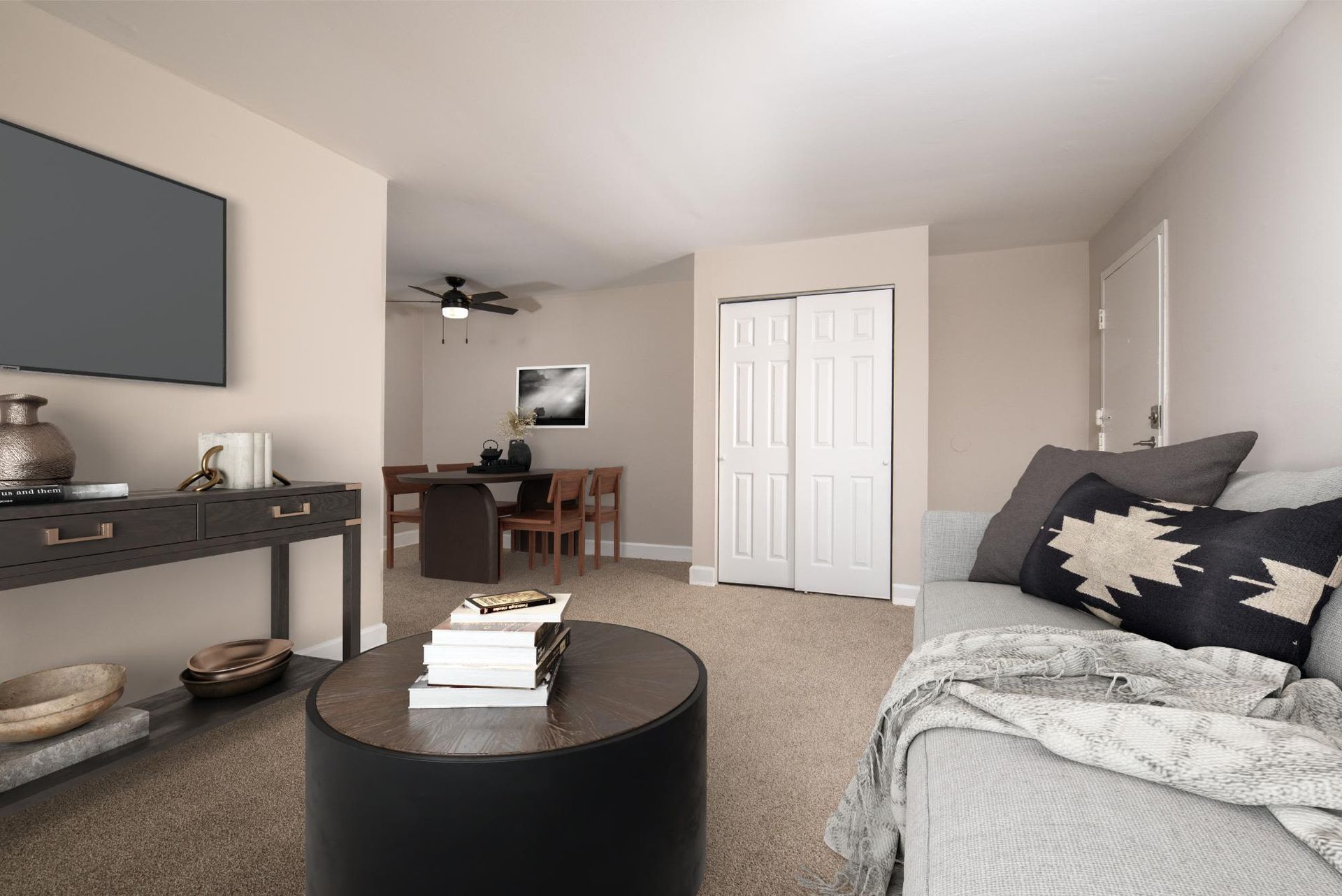 Living room in an apartment with a gray sofa, round coffee table, TV, and dining area at Liberty Pointe in Newark, DE.