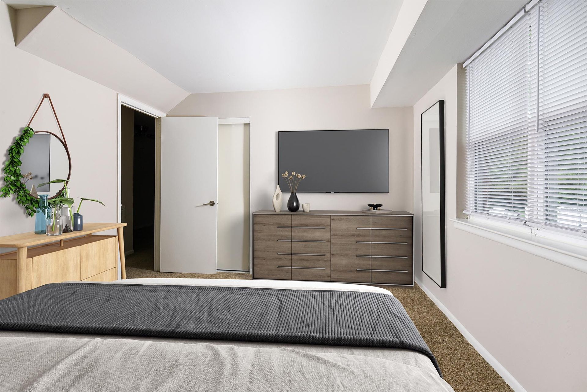 Bedroom in a modern apartment with a dresser, TV, and window blinds at Liberty Pointe in Newark, DE.