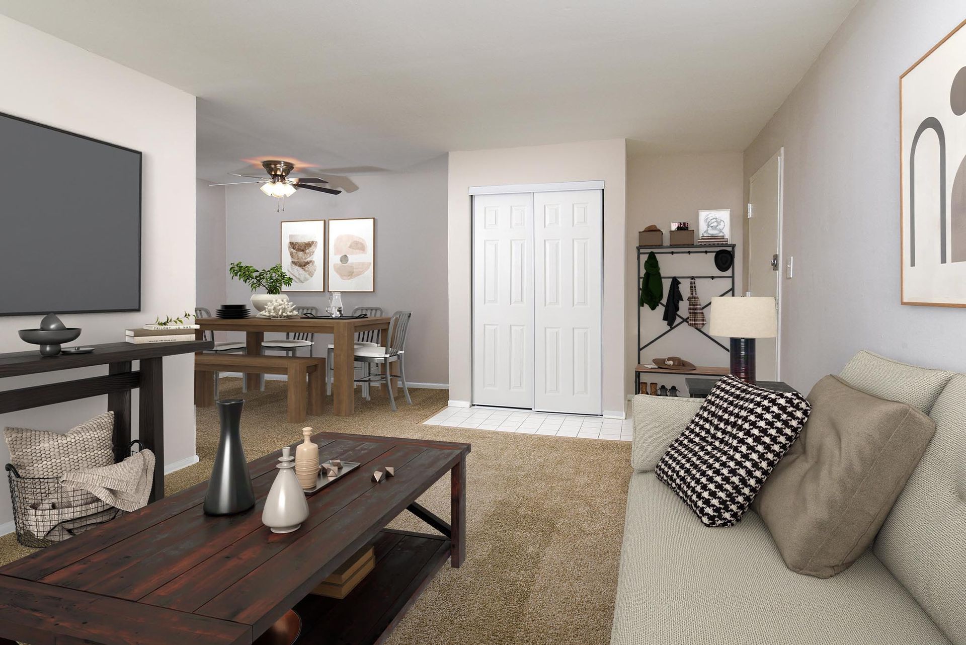 Interior living room with beige walls, a wall-mounted TV, sofa, coffee table, dining table, and a coat closet at Liberty Pointe in Newark, DE.