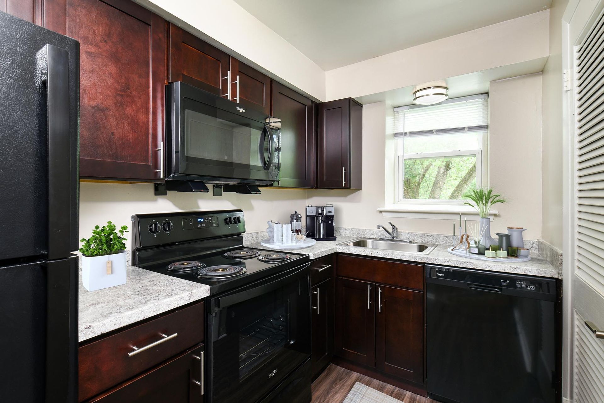 Kitchen with dark wood cabinets, black stove and microwave, granite countertops, and a window over the sink at Liberty Pointe in Newark, DE.