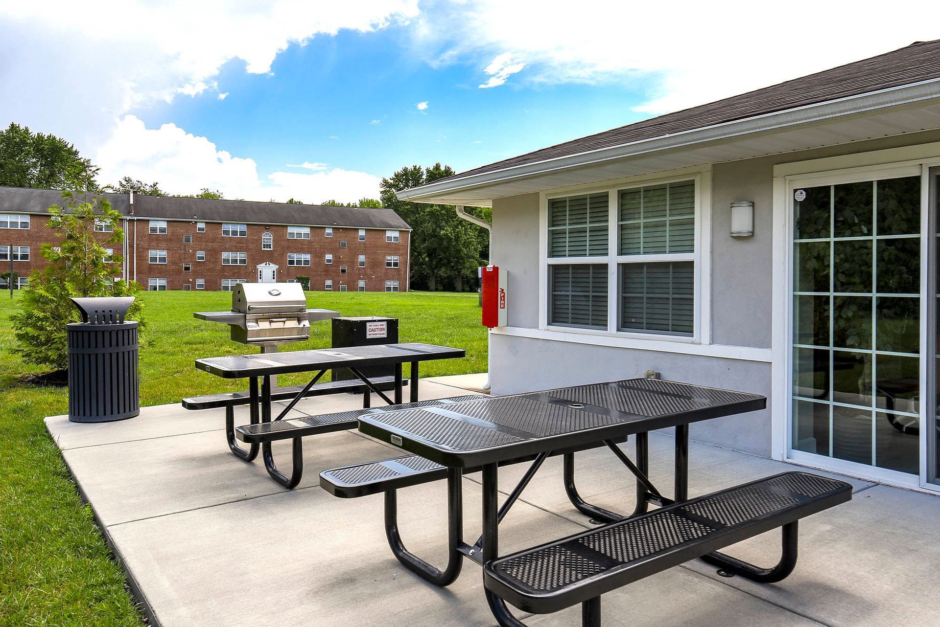 Outdoor communal grilling area with two metal picnic tables, a grill, and a nearby apartment building at Liberty Pointe in Newark, DE.