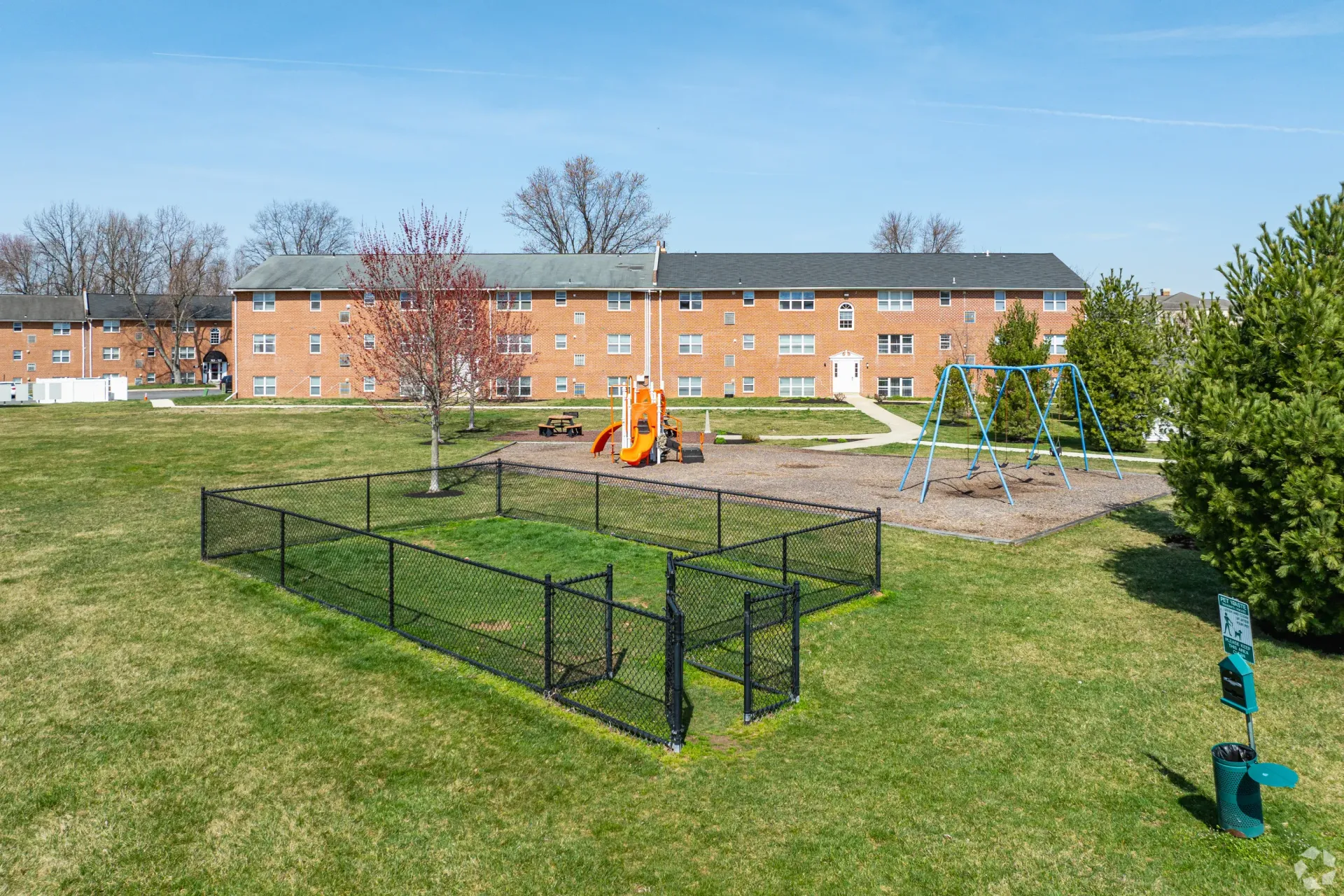 Open green lawn with a playground and swings, surrounded by brick apartment buildings at Liberty Pointe in Newark, DE.