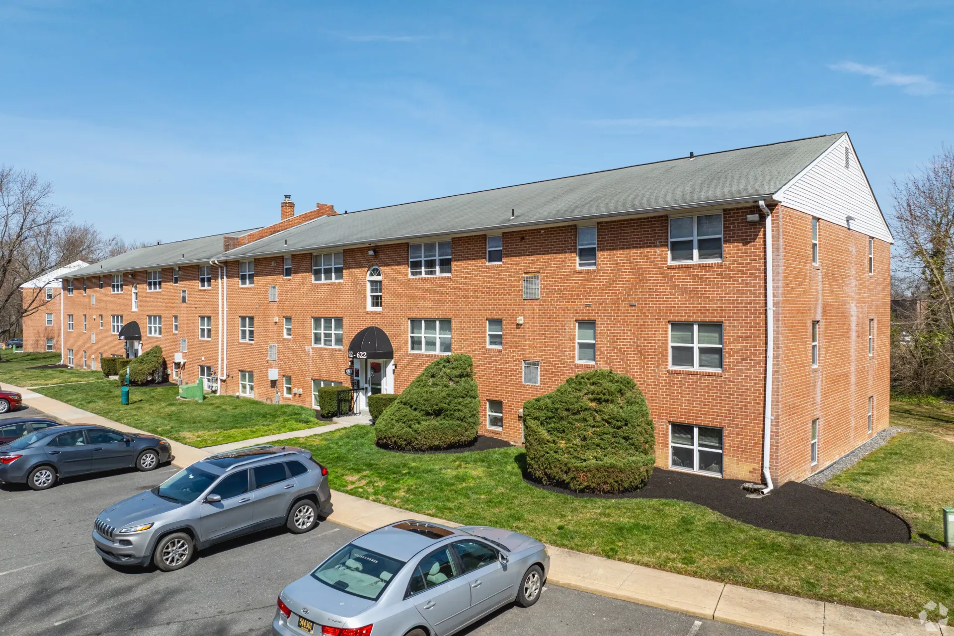 Exterior view of a brick apartment building with a parking lot and landscaping at Liberty Pointe in Newark, DE.