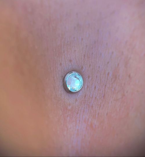 Close-up of skin with a dermal piercing, featuring a small, round, opalescent stud.