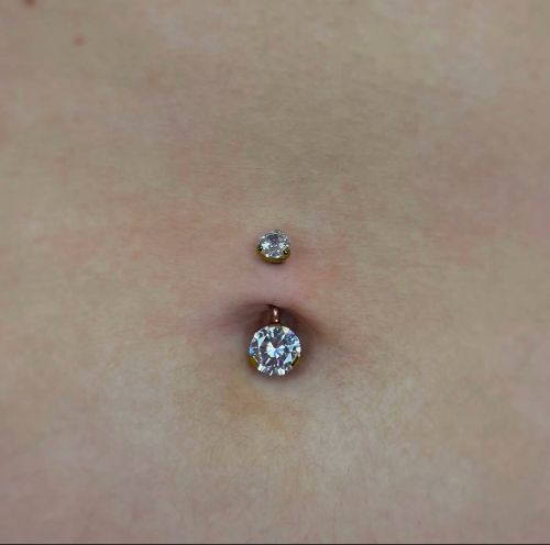 Belly button pierced with two silver gem studs on skin.