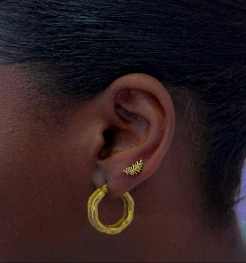 Close-up of person's ear with a small leaf stud and textured gold hoop earring.