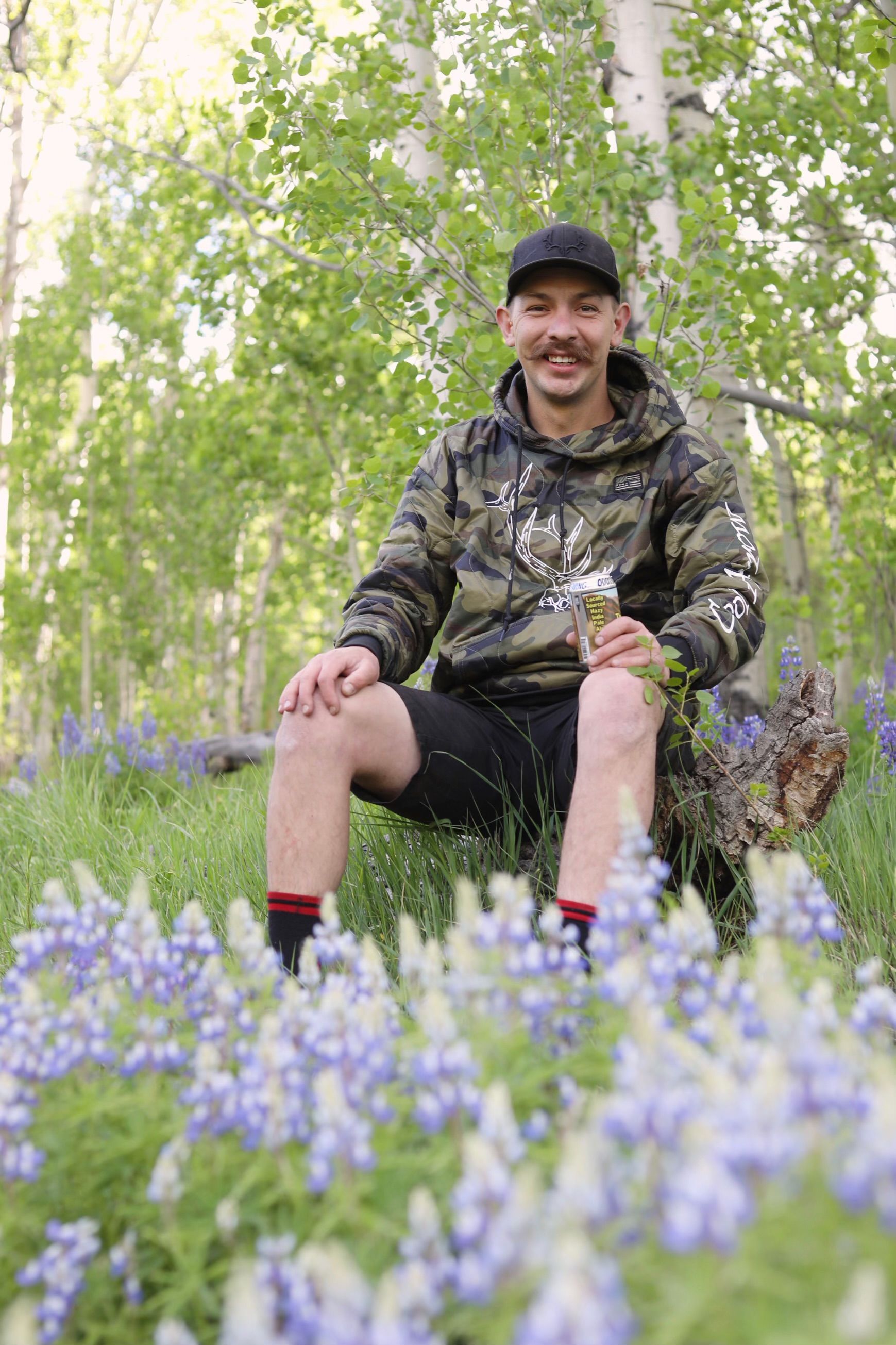 A man is sitting on a log in the middle of a field of flowers.