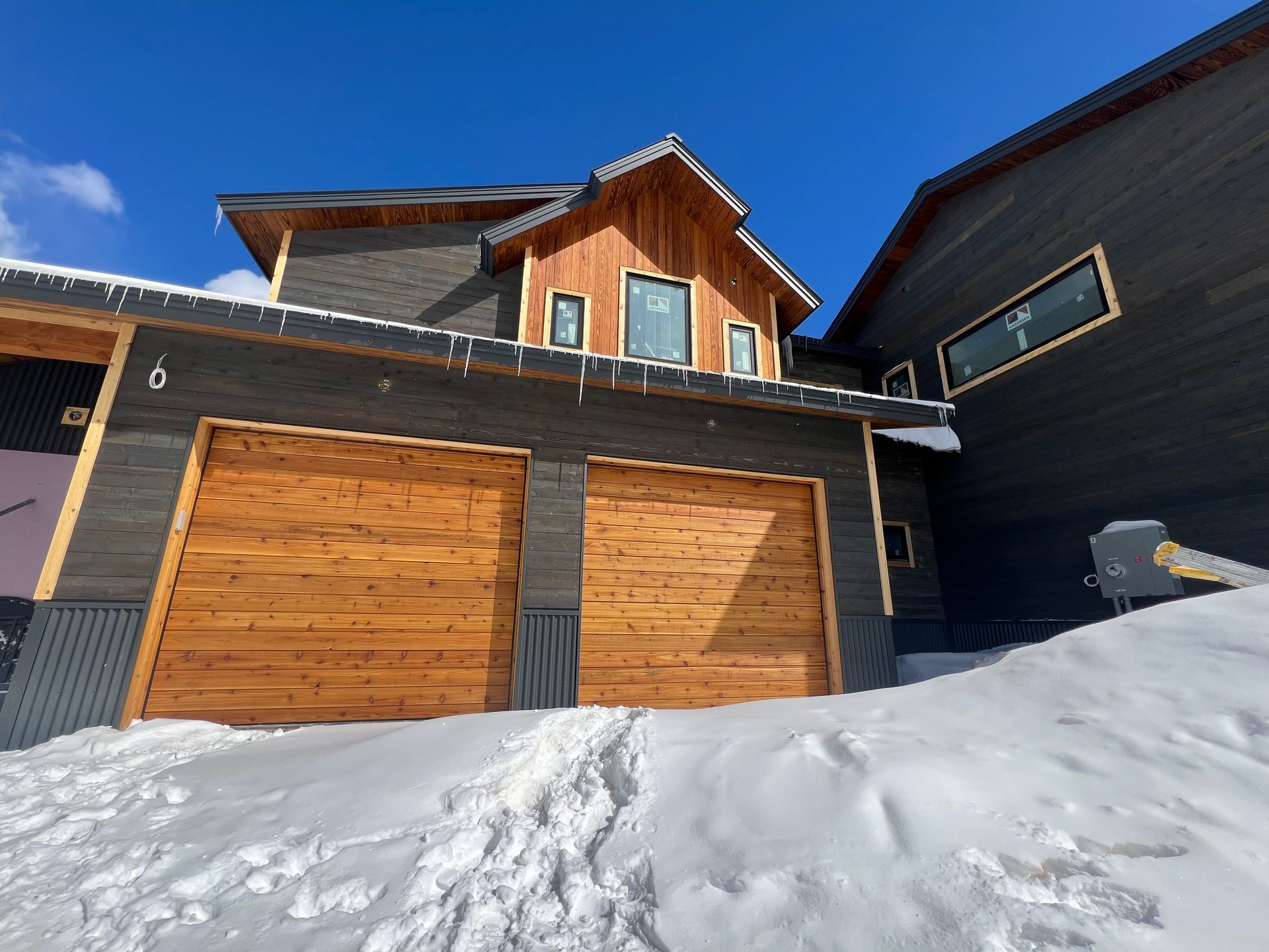 A house with two wooden garage doors is covered in snow.