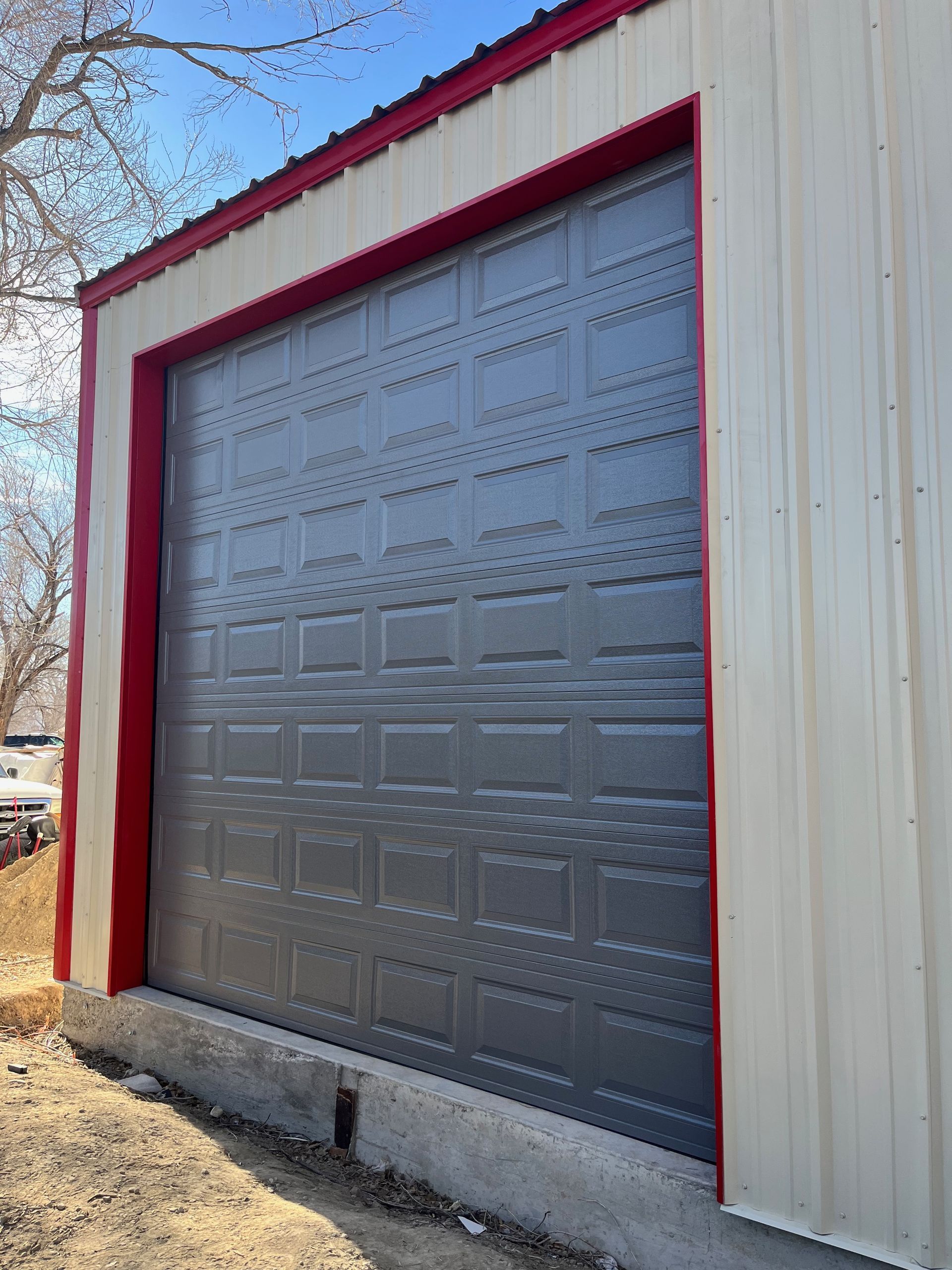 A gray garage door with a red trim on a white building.