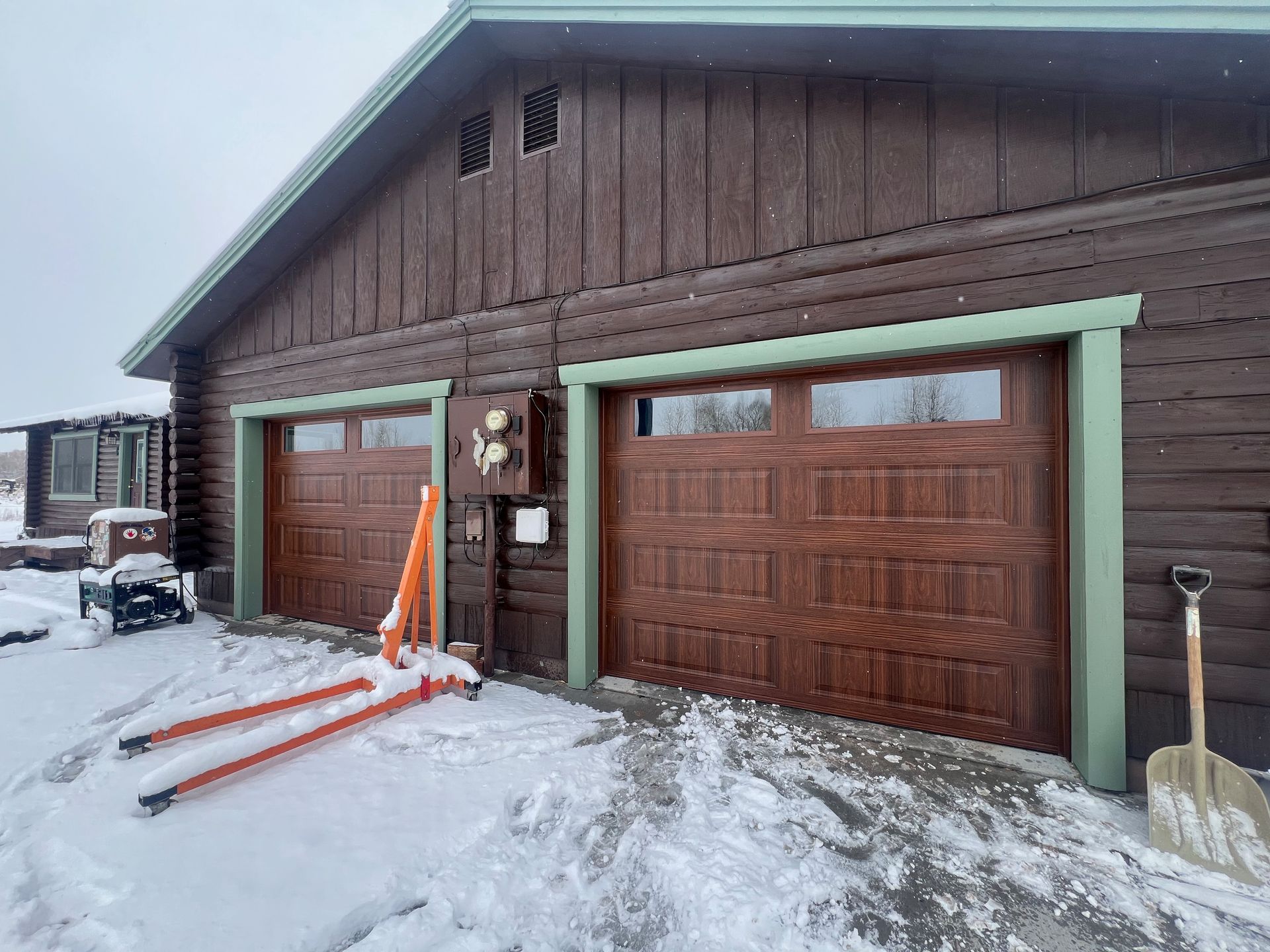 A log cabin with three garage doors in the snow.