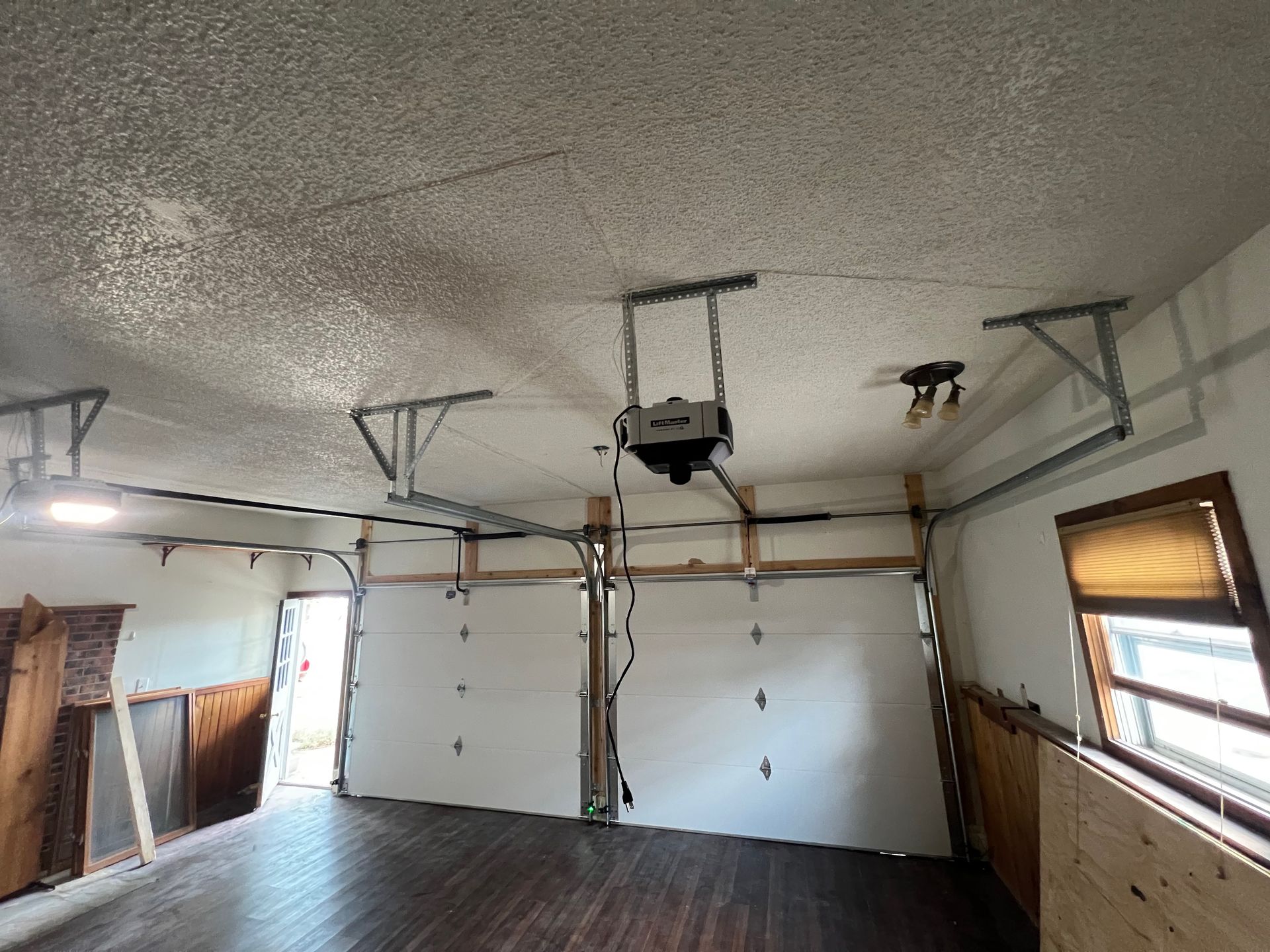 Interior view of a garage with two white garage doors, a ceiling-mounted opener, and a wood-paneled interior.
