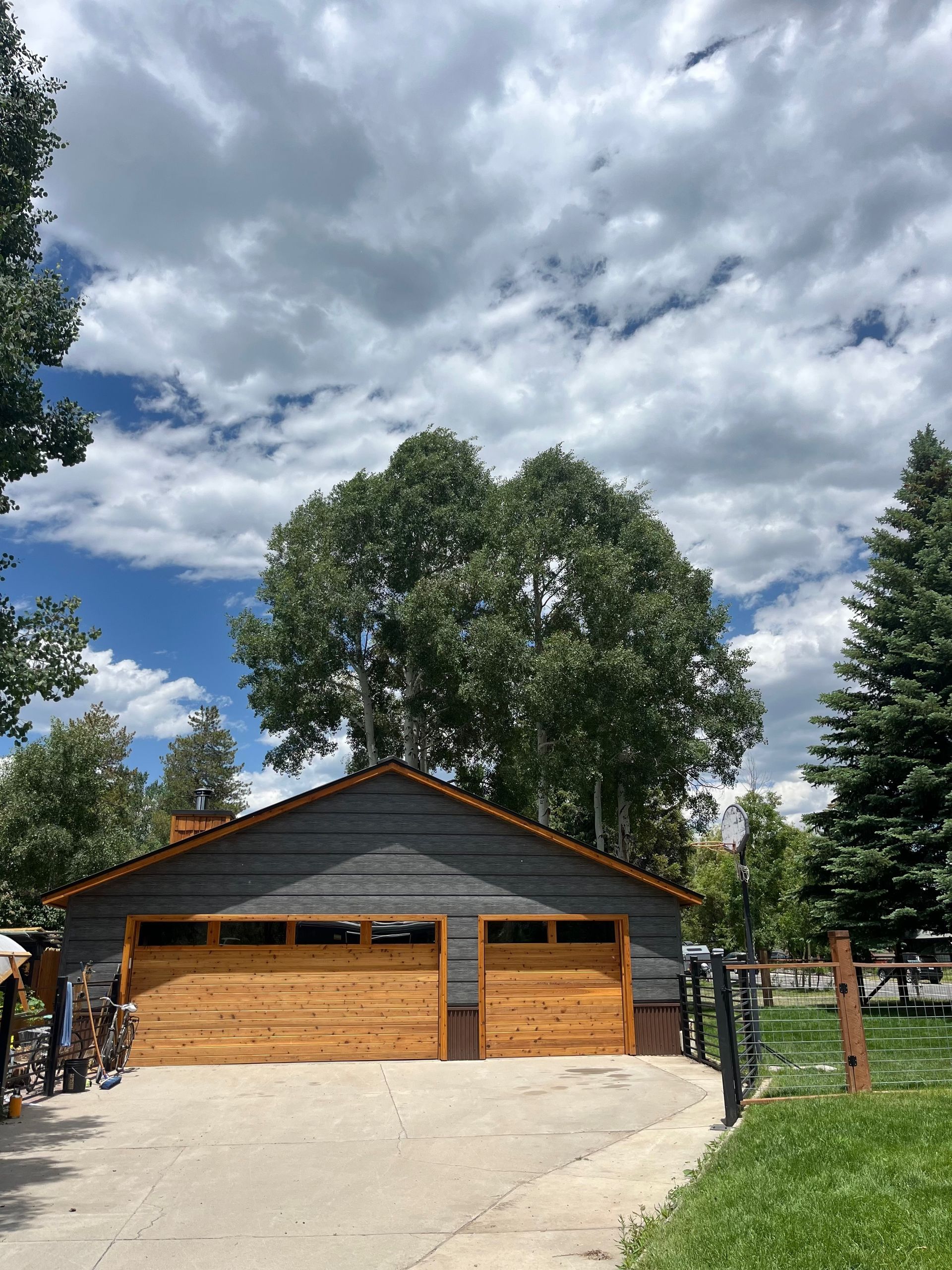 Two-car garage with light wood doors and dark gray siding, under a partly cloudy sky.
