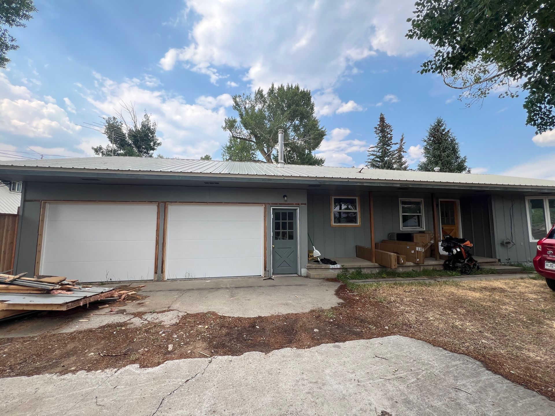 A gray house with a two-car garage and a small door. Construction materials are scattered in the yard.