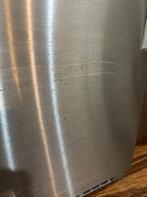a close up of a dirty stainless steel refrigerator door with stains and rust on it .