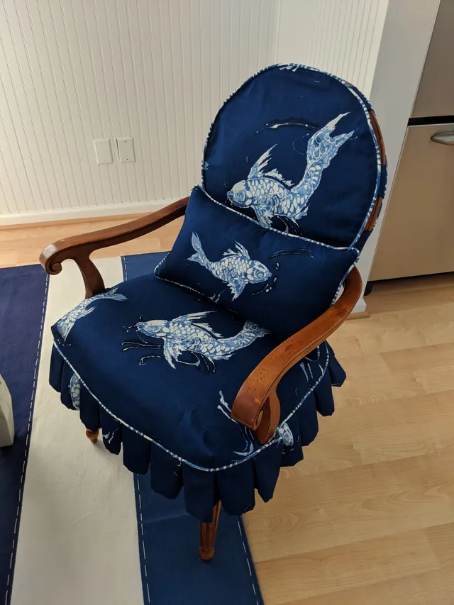 Blue chair with koi fish print, wooden arms, and a small pillow; set on a blue and white rug.