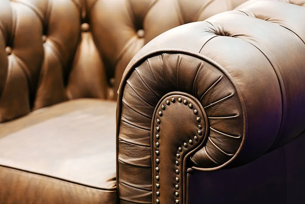 Brown leather Chesterfield sofa arm with button tufting and studded trim.