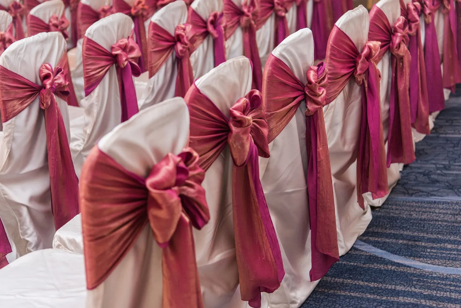White chairs with maroon sashes and bows arranged in rows for an event.