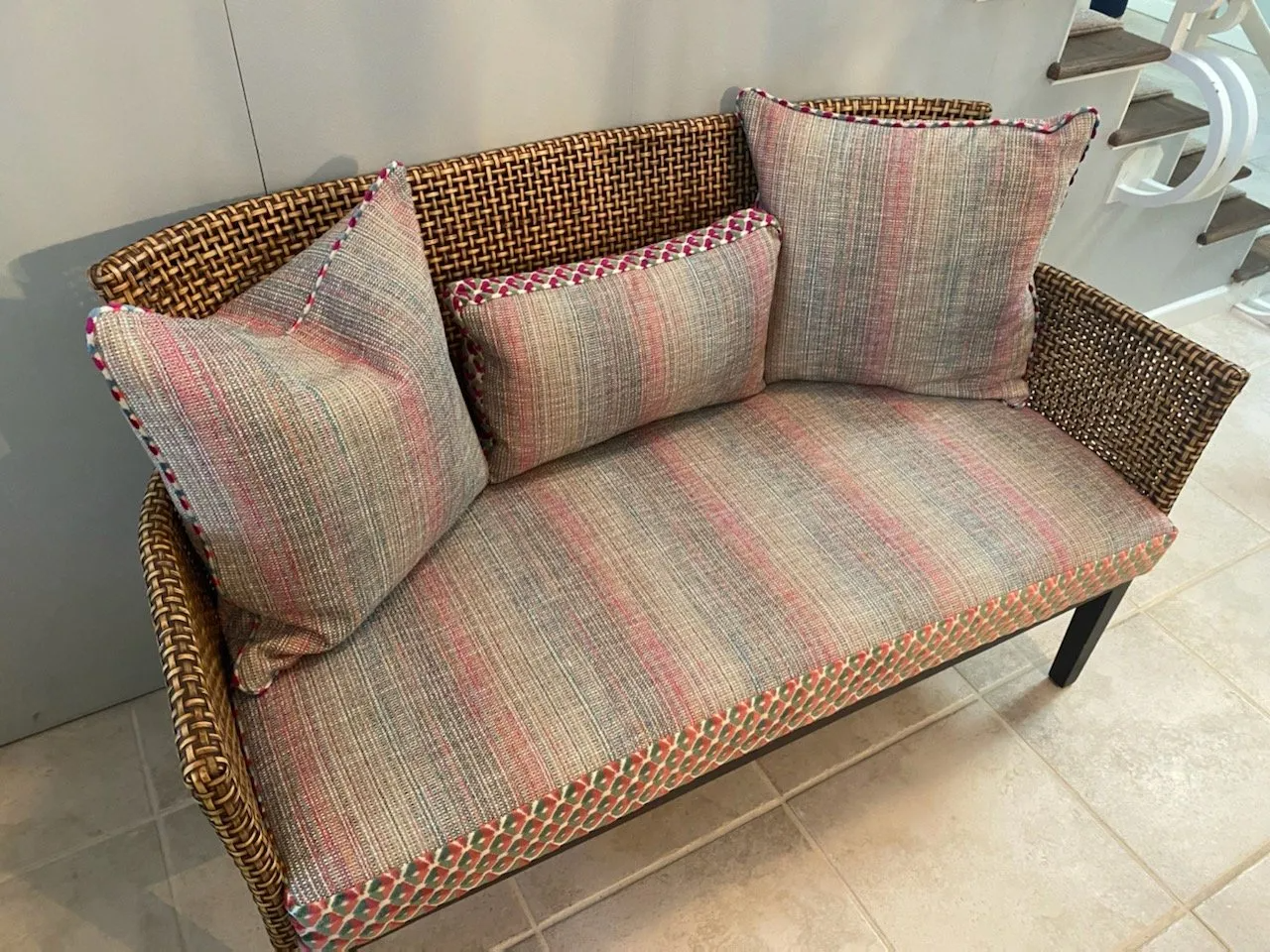 Wicker loveseat with gray and pink striped cushions and pillows; white stairs in background.