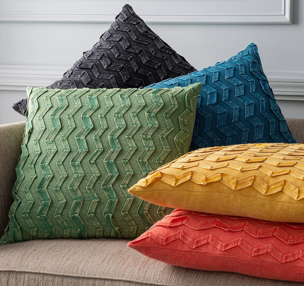 Pile of decorative throw pillows in various colors: green, yellow, orange, dark blue, and black.