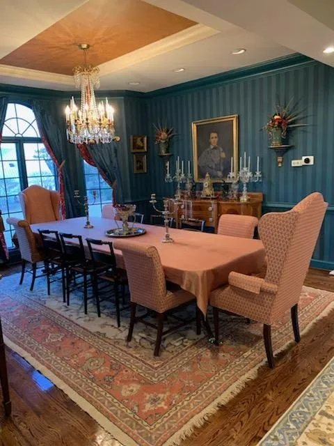 Formal dining room with teal striped walls, ornate chandelier, long table set for a meal, and antique furniture.