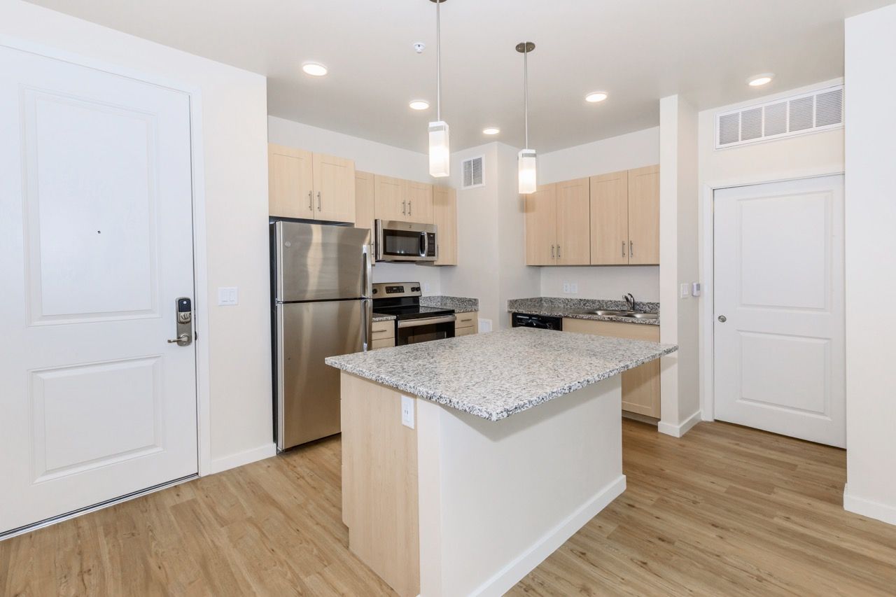 Bright modern kitchen with granite island, stainless steel appliances and light wood cabinets.