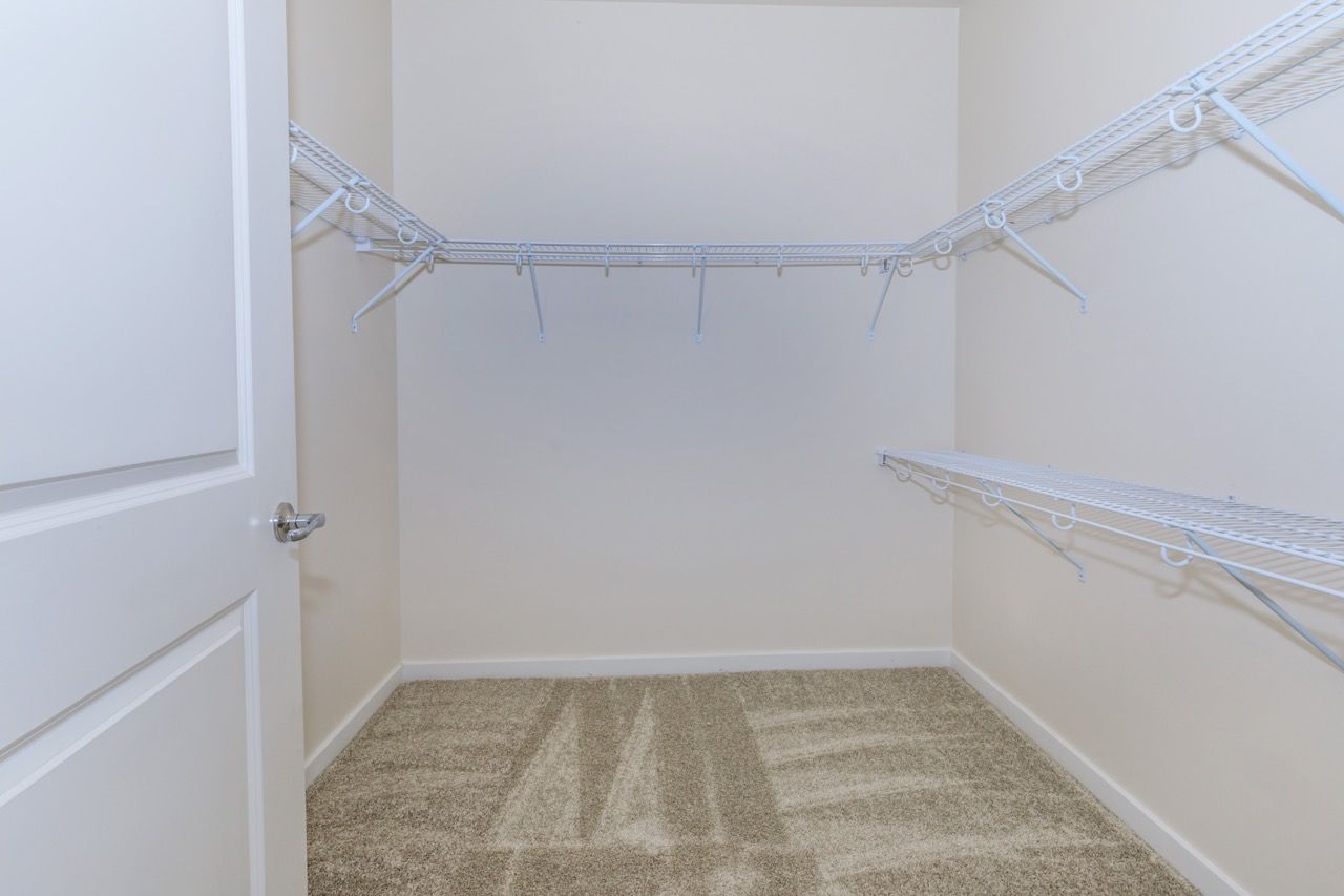 Empty walk-in closet with white wire shelves and beige walls.