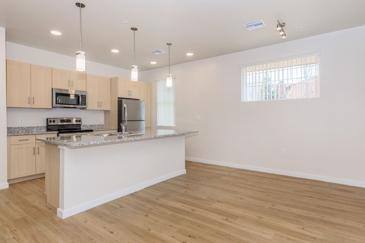 Open-concept kitchen with granite island, light wood cabinets, and stainless steel appliances.