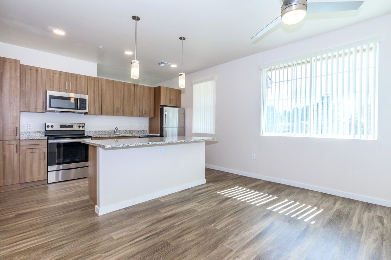 Open kitchen with granite counters, wooden cabinets, an island, and a large window with blinds.