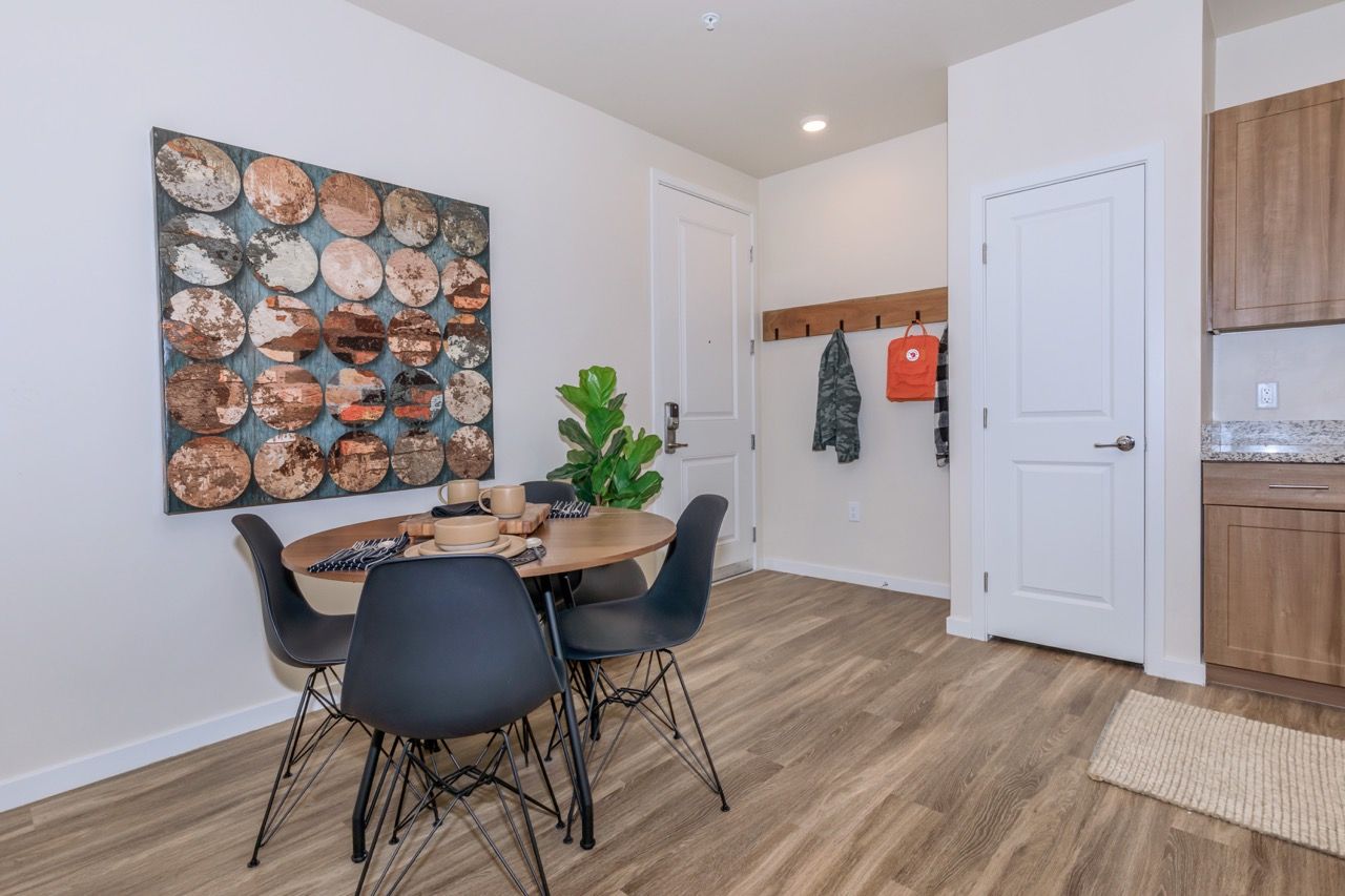 Dining area with a round wood table, four chairs, wall art, and a coat rack by the entry.
