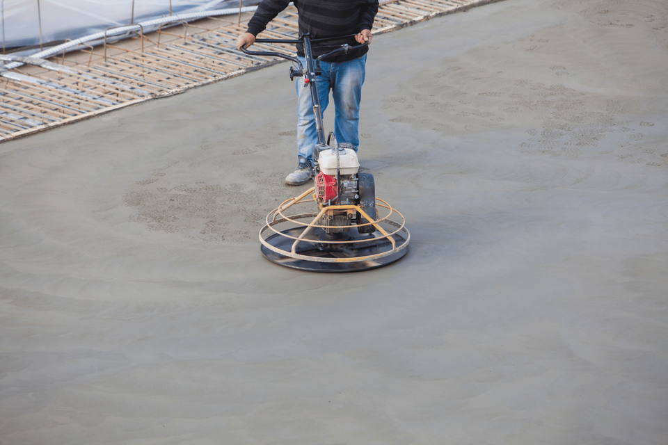 A man is using a machine to finish concrete on a construction site.