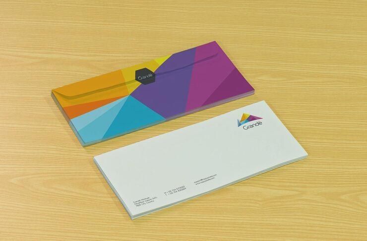 Two colorful business envelopes on a wooden surface; one sealed, one open.
