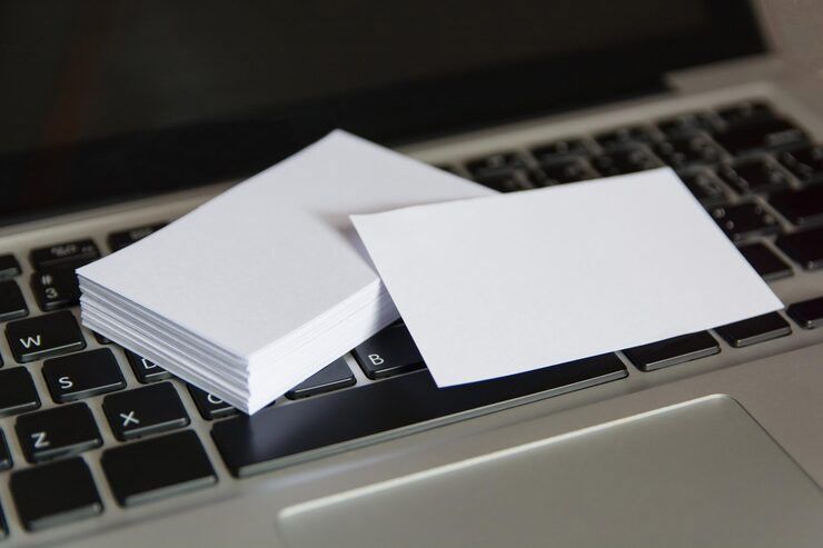 White business cards stacked and next to one card, resting on a laptop keyboard.