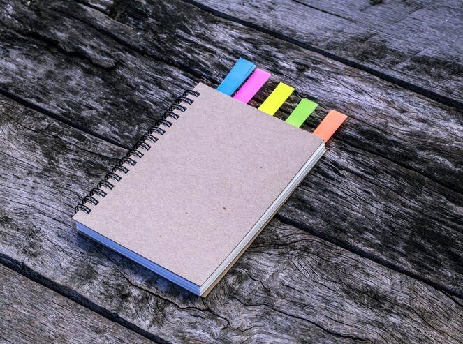 Spiral notebook with colorful sticky tabs on a weathered wood surface.