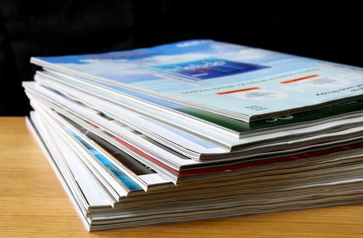 Stack of magazines on a wooden surface, with colorful covers visible.