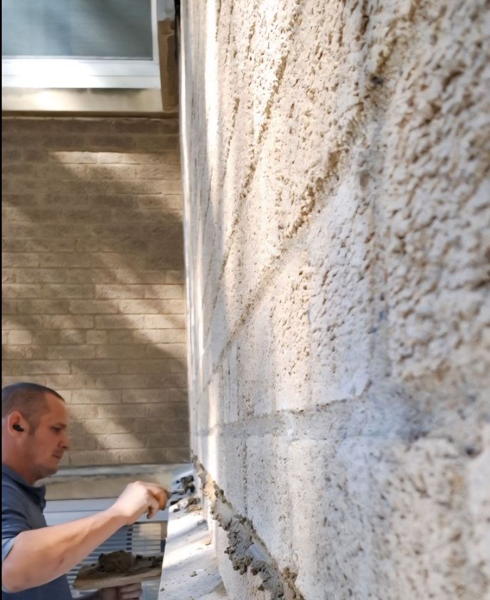 Man applies stucco to a wall. Exterior setting, daytime.