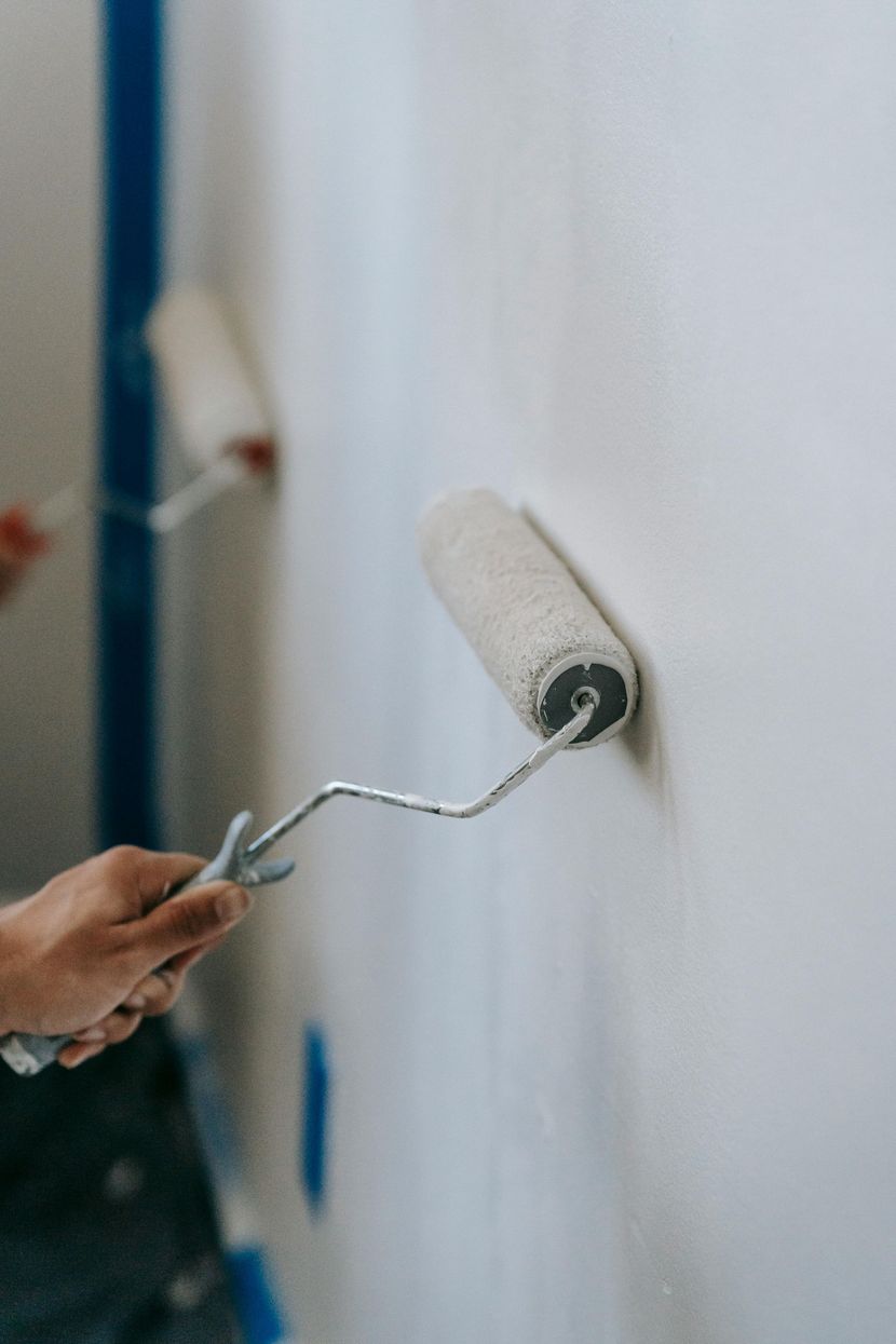 Hand using paint roller to apply white paint on a wall.