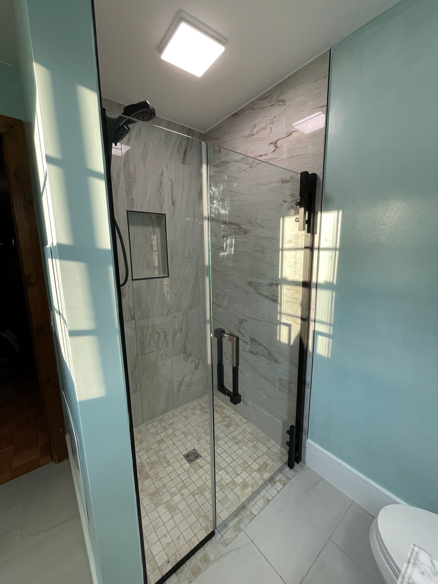 Glass shower enclosure in a tiled bathroom with teal walls and white floor.
