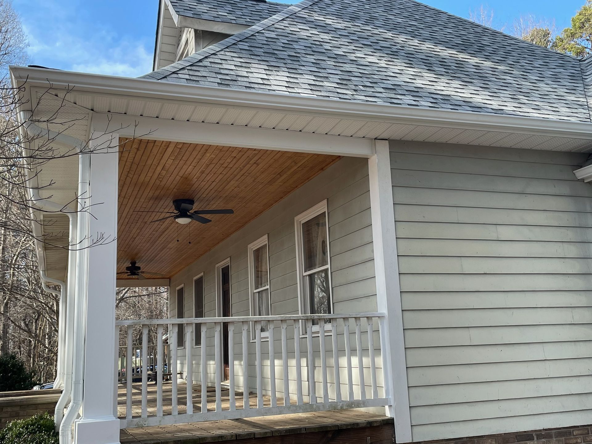 Front porch with white railings, tan ceiling, ceiling fan, and gray siding on a house