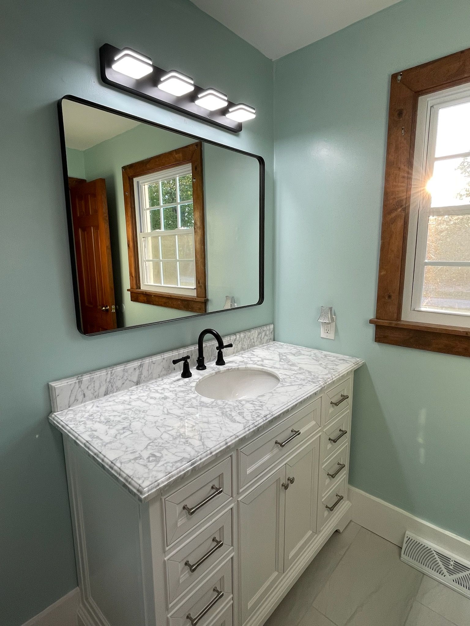 Bathroom vanity with white marble countertop, black faucet, wall mirror, and mint green walls.