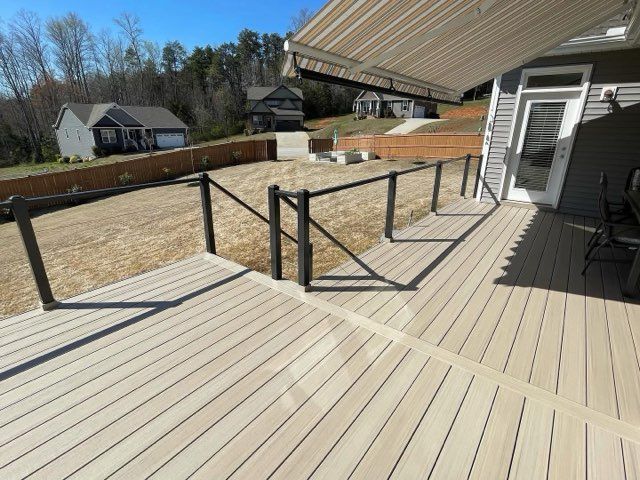 Spacious deck with black railing, light wood boards, and a sloped roof beside a house and yard