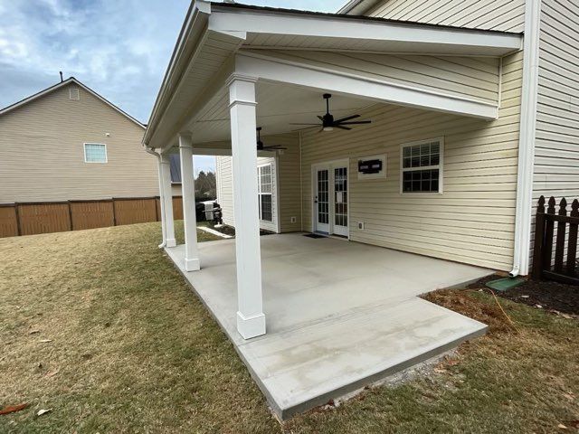 Covered concrete patio with white columns and ceiling fan beside a beige house