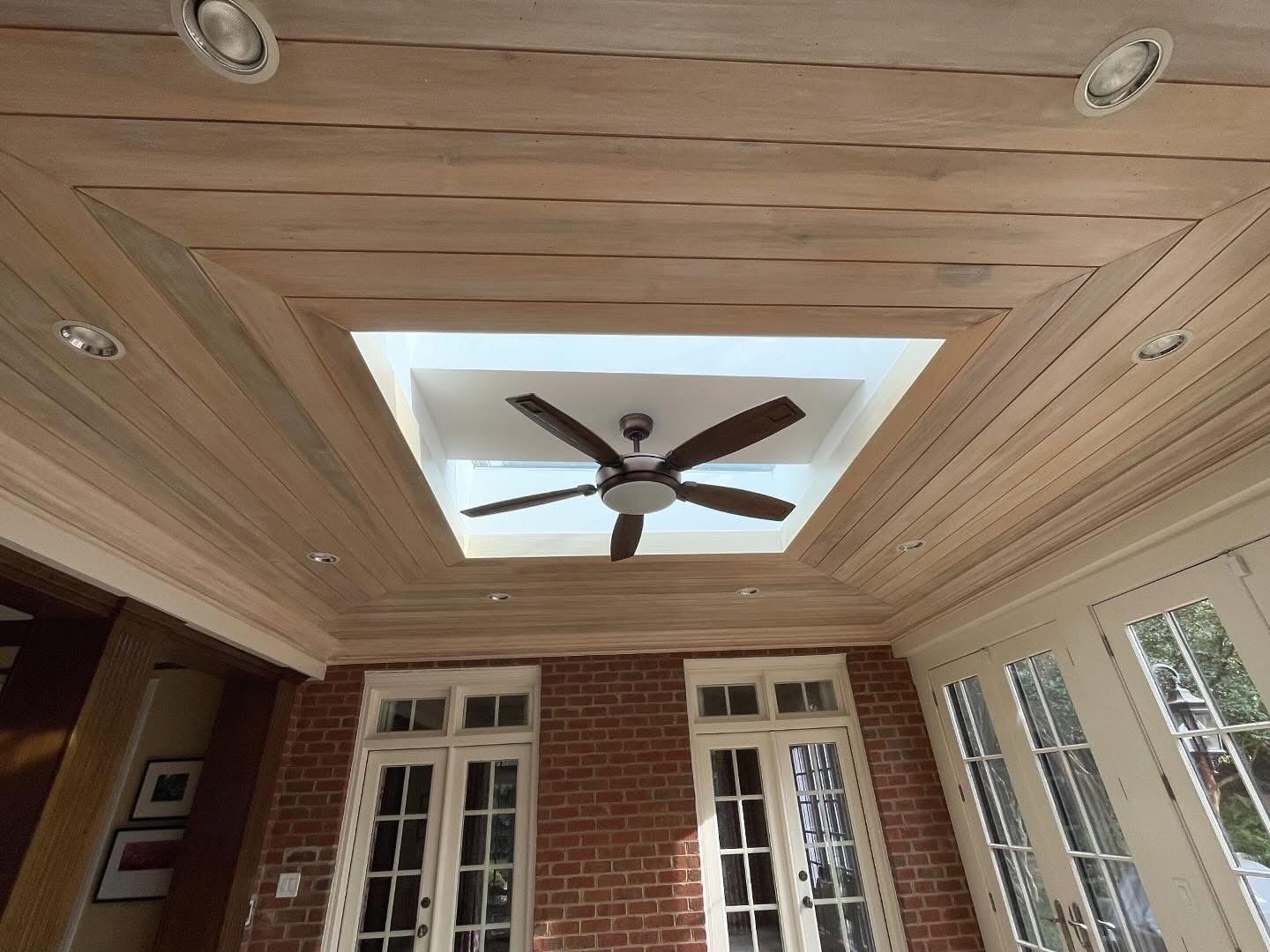 Wood-paneled porch ceiling with recessed lights and a ceiling fan above brick and French doors