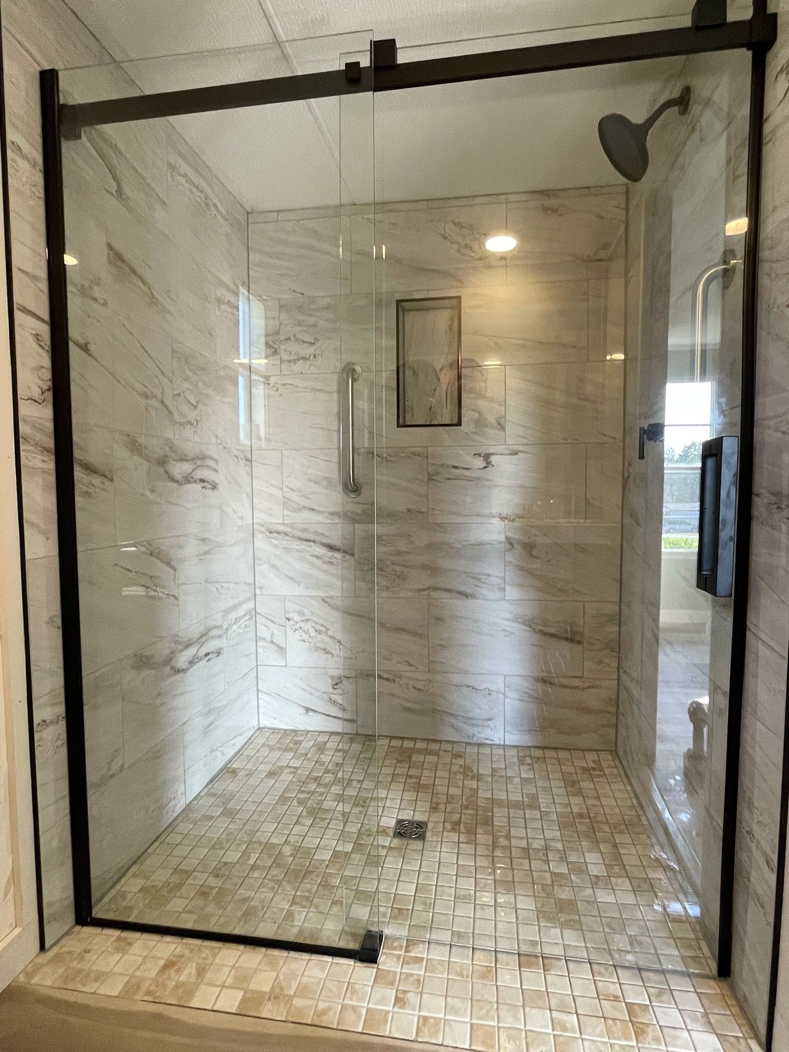 Glass-enclosed marble-tiled walk-in shower with rainfall showerhead and mosaic floor.
