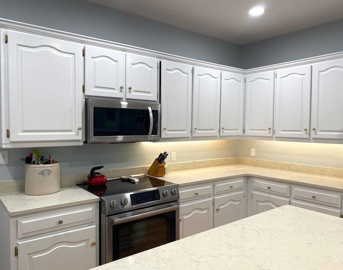 Bright modern kitchen with white cabinets, stainless oven and microwave, and under-cabinet lighting.