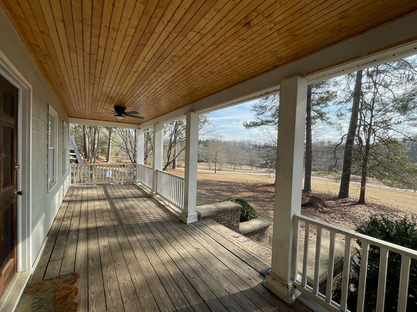 Covered wooden porch with white railings overlooking a rural yard and open field