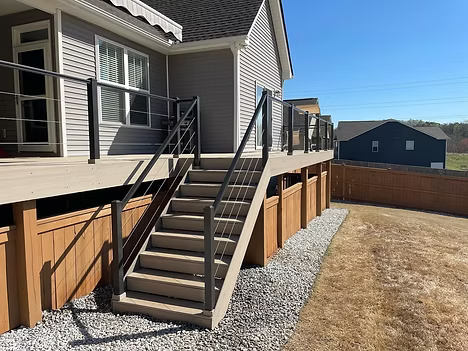 House deck with black-railed stairs and beige siding beside a gravel yard and wooden fence.