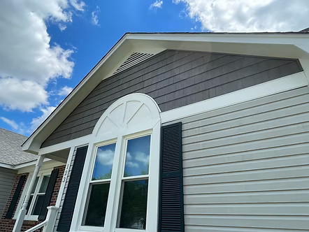 Exterior of a house with gray siding, white trim, and an arched window under a blue sky