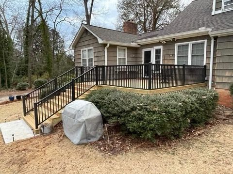 House exterior with black railing ramp, beige siding, and covered grill by a shrub-covered porch